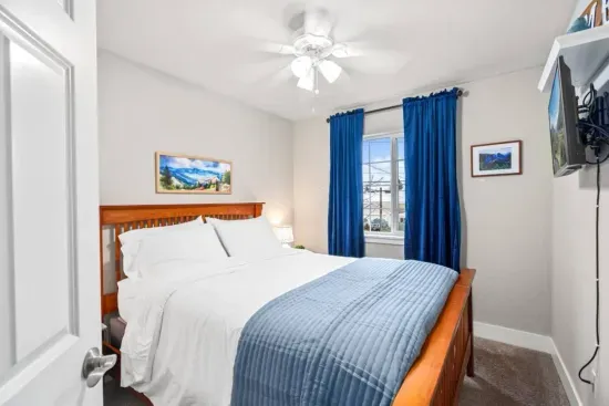 BEDROOM 3: Queen size bed, similar setup with nightstands, lamps, blackout curtains, phone charging cable, luggage rack, ceiling fan, clothes hangers, laundry hamper.