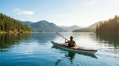 Kayaker enjoys a serene lake surrounded by pine-covered mountains