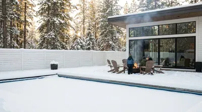 Family warms by outdoor fire pit next to snowy pool