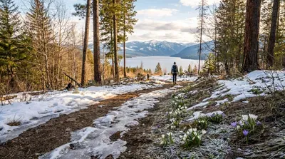 Hiker on snowy trail overlooking beautiful lake and mountains