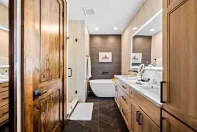 A luxurious primary bathroom with ample space for both to get ready. Enjoy a full-size soaking tub, oversized shower, floor-to-ceiling designer tile, and a lighted mirror with a built-in Bluetooth speaker and weather station to kickstart your day.