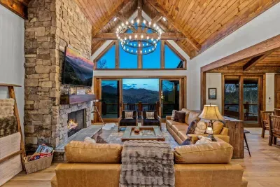 Spacious family room with plush leather sofas, a 75" smart TV, and a cozy fireplace. Enjoy breathtaking mountain views through the window wall with sliding glass doors, offering a perfect blend of comfort and natural beauty.