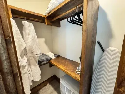 A walk-in closet is provided with 2 plush robes, a clothing hamper, iron and ironing board, plenty of space to hang items, and extra blankets, pillows and towels.