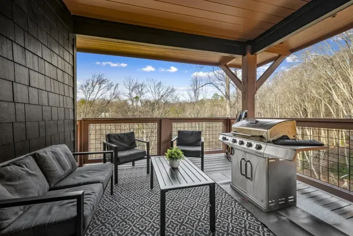Covered deck with cushioned seating, stainless steel grill, and a nice view.