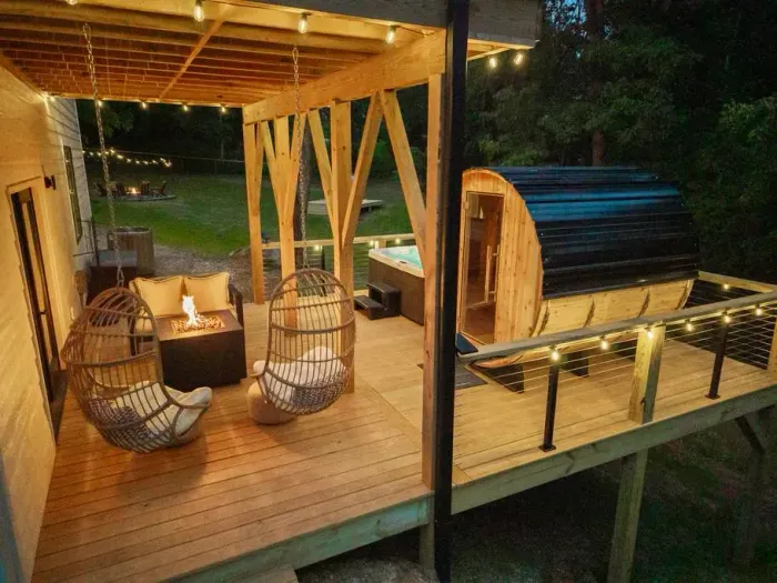 Kick back on the basket swings, relax in the hot tub or barrel sauna, and enjoy the fire pit. It’s a cozy evening setting with string lights that make the whole deck feel just right.