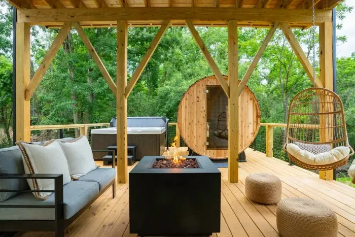 Unwind on the back deck with a 6-person hot tub, barrel sauna, cozy propane fire pit, seating area, and hanging swings.