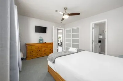 This space seamlessly blends style and function, featuring a light wood bed frame and dresser set. With a ceiling fan, a flat-screen TV, and easy access to both the closet and an en-suite bathroom, every detail is covered for a perfect stay.