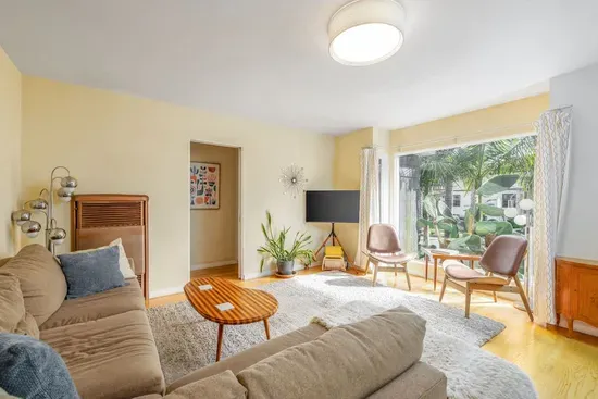 Sun-Soaked Ambiance: Large windows fill the room with natural light, highlighting the warm tones of the hardwood floors and wooden cabinetry.
