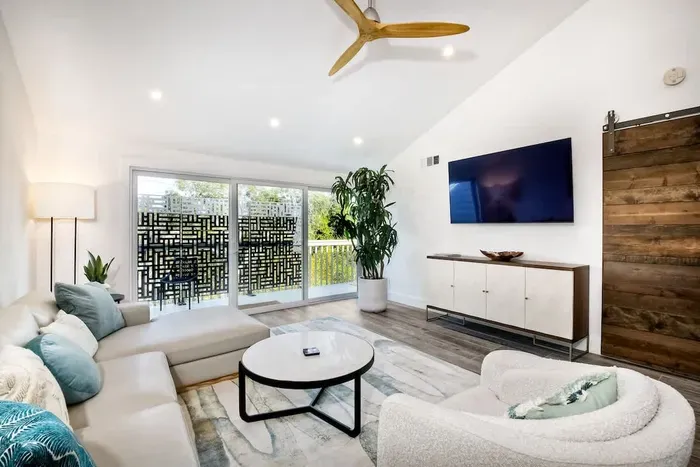 The space is well-lit with recessed ceiling lights and natural light streaming in from large sliding glass doors, which lead to an outdoor patio with decorative privacy panels.
