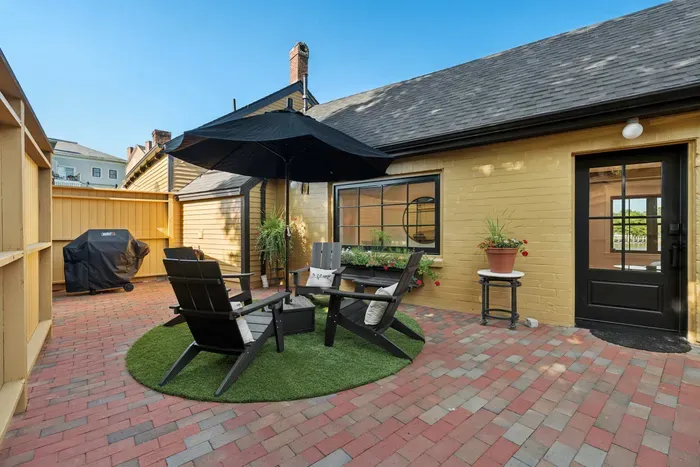 Outdoor courtyard featuring four Adirondack chairs and an umbrella. There is also a webber gas grill.