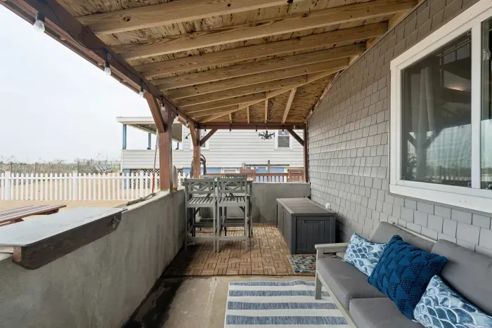 Covered front porch on the sand with dining table and small outdoor sofa