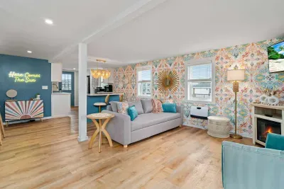 Open, living room, kitchen & dining room with "here comes the sun" neon light sign, flat screen smart TV & sleeper sofa. Private front covered deck with seating, back private deck with picnic table, yoga mats, dining table for 6 pp &  island for 2pp
