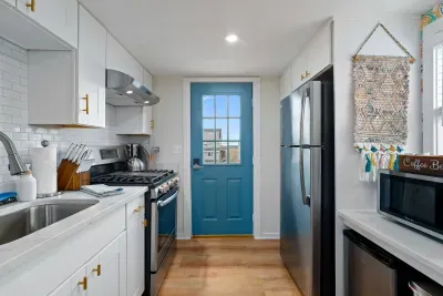 Open, living room, kitchen & dining room with "here comes the sun" neon light sign, flat screen smart TV & sleeper sofa. Private front covered deck with seating, back private deck with picnic table, yoga mats, dining table for 6 pp &  island for 2pp