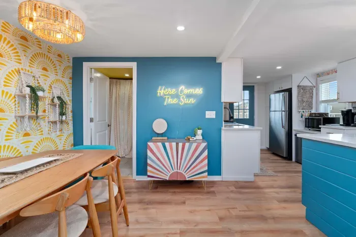 Open, living room, kitchen & dining room with "here comes the sun" neon light sign, flat screen smart TV & sleeper sofa. Private front covered deck with seating, back private deck with picnic table, yoga mats, dining table for 6 pp &  island for 2pp