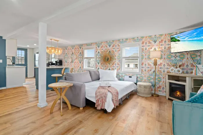 Living room/kitchen #2, on the 2nd level, with "here comes the sun" neon light sign, flat screen smart TV & sleeper sofa. Private front covered deck with seating, back private deck with picnic table, yoga mats, dining table for 6 pp & island for 2pp