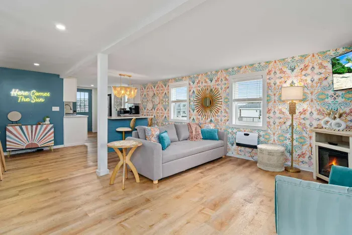 Living room/kitchen #2, on the 2nd level, with "here comes the sun" neon light sign, flat screen smart TV & sleeper sofa. Private front covered deck with seating, back private deck with picnic table, yoga mats, dining table for 6 pp & island for 2pp