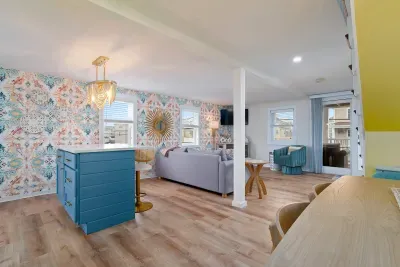 Living room/kitchen #2, on the 2nd level, with "here comes the sun" neon light sign, flat screen smart TV & sleeper sofa. Private front covered deck with seating, back private deck with picnic table, yoga mats, dining table for 6 pp & island for 2pp
