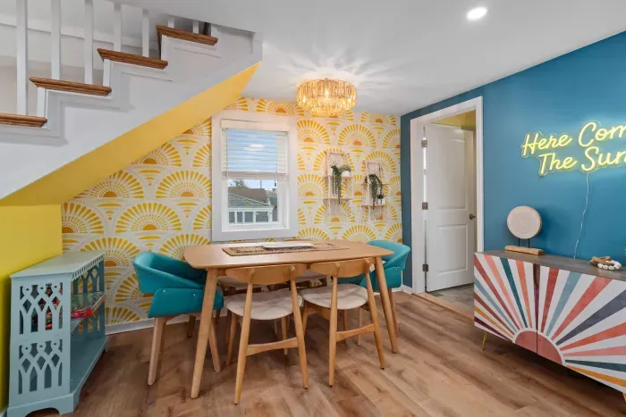 Living room/kitchen #2, on the 2nd level, with "here comes the sun" neon light sign, flat screen smart TV & sleeper sofa. Private front covered deck with seating, back private deck with picnic table, yoga mats, dining table for 6 pp & island for 2pp