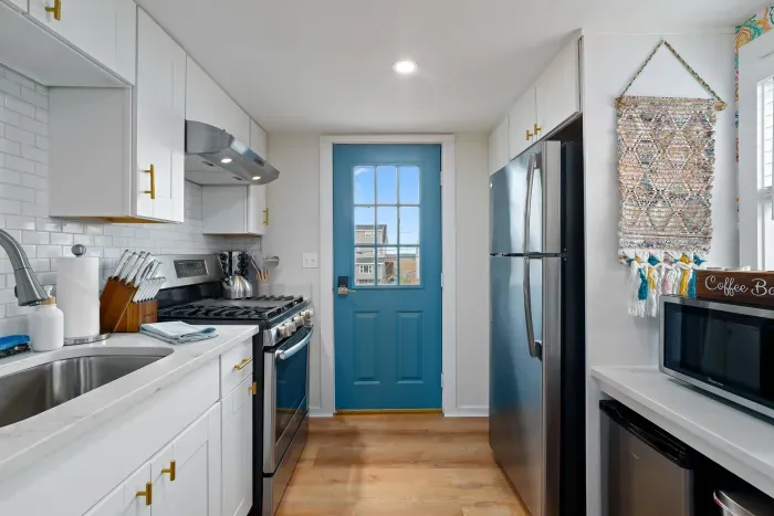 Living room/kitchen #2, on the 2nd level, with "here comes the sun" neon light sign, flat screen smart TV & sleeper sofa. Private front covered deck with seating, back private deck with picnic table, yoga mats, dining table for 6 pp & island for 2pp