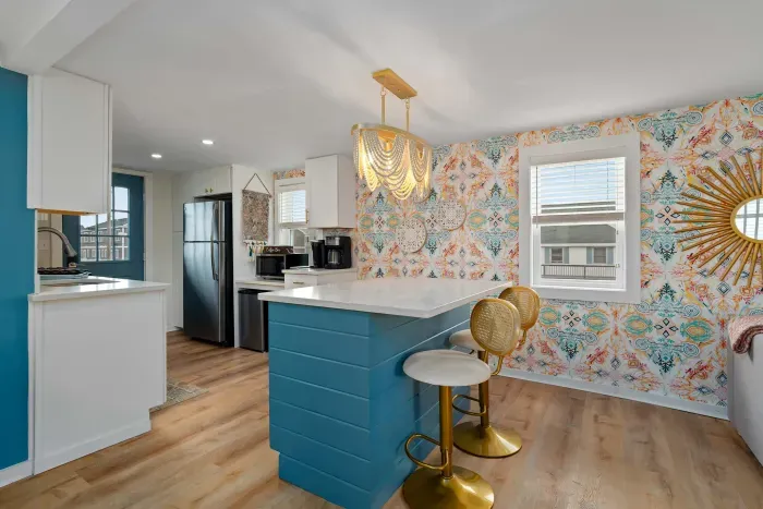 Living room/kitchen #2, on the 2nd level, with "here comes the sun" neon light sign, flat screen smart TV & sleeper sofa. Private front covered deck with seating, back private deck with picnic table, yoga mats, dining table for 6 pp & island for 2pp