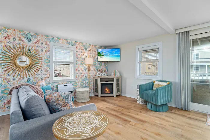 Living room/kitchen #2, on the 2nd level, with "here comes the sun" neon light sign, flat screen smart TV & sleeper sofa. Private front covered deck with seating, back private deck with picnic table, yoga mats, dining table for 6 pp & island for 2pp