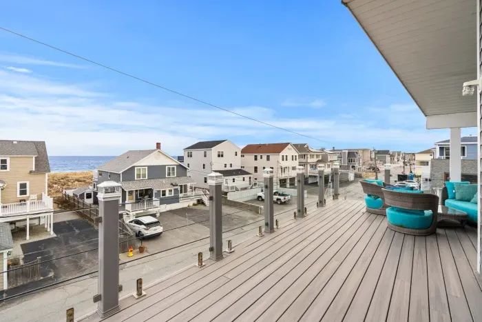 Top-floor deck with outdoor furniture including a swing, unreal oceans views, and glass railings.