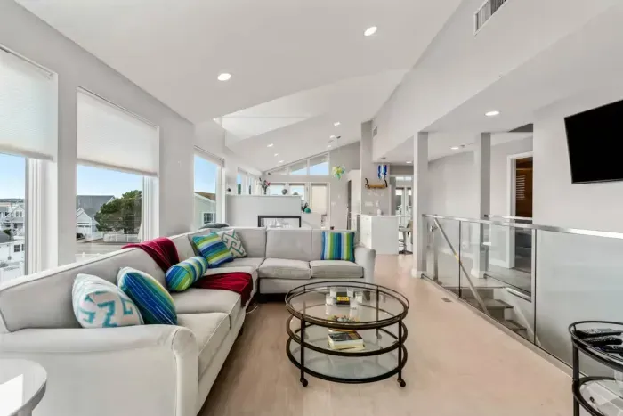 The Penthouse - Bright and modern living space featuring floor-to-ceiling windows, stylish décor, and an open layout perfect for relaxing or entertaining. The spacious sectional, colorful accents, and sleek finishes create a welcoming coastal vibe.