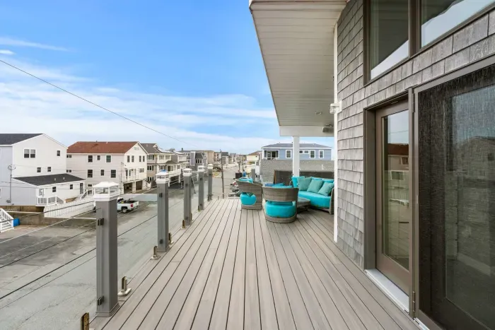 Top-floor deck with outdoor furniture including a swing, unreal oceans views, and glass railings. Accessed via the primary bedroom and the living room