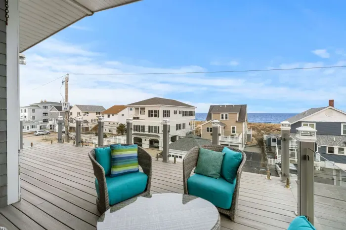 Top-floor deck with outdoor furniture including a swing, unreal oceans views, and glass railings.