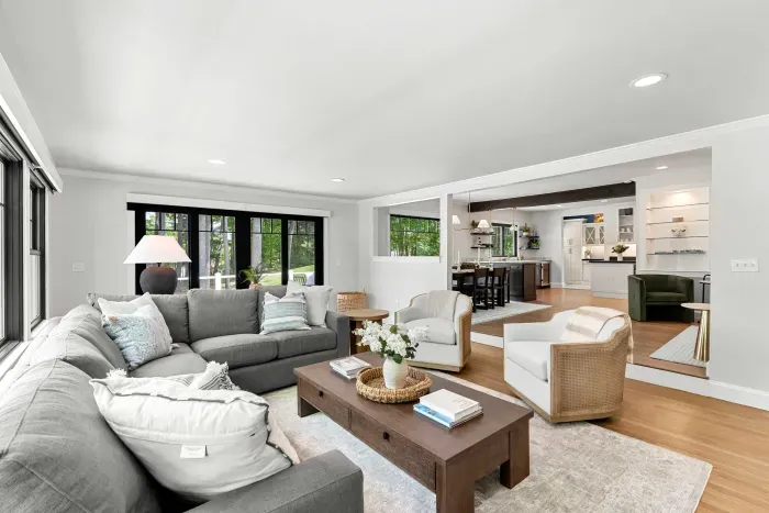 The heart of the home. A sprawling sectional, smart TV, and two lounge chairs — plus sliders that blur the line between inside and out, opening to a stunning creekside deck