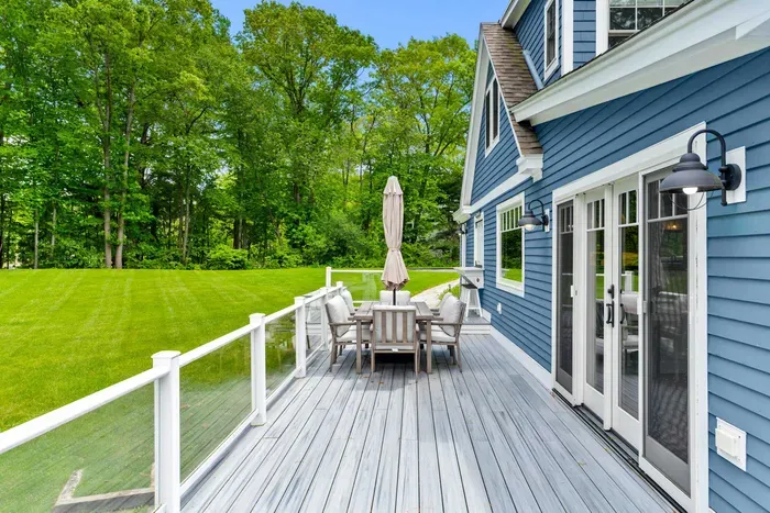 Deck with bar seating for three, a six-person outdoor dining table with umbrella, and a gas grill for guest use.