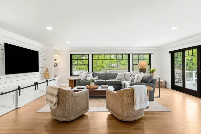 The heart of the home. A sprawling sectional, smart TV, and two lounge chairs — plus sliders that blur the line between inside and out, opening to a stunning creekside deck.