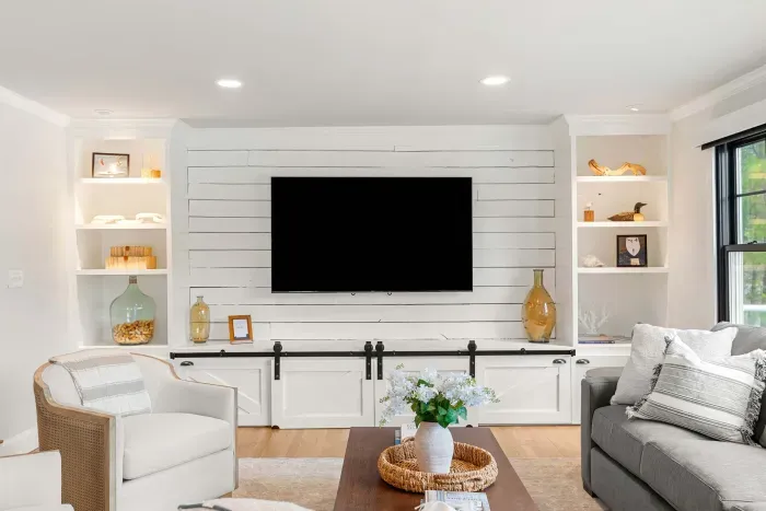 The heart of the home. A sprawling sectional, smart TV, and two lounge chairs — plus sliders that blur the line between inside and out, opening to a stunning creekside deck.