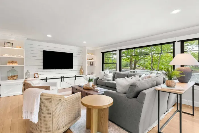 The heart of the home. A sprawling sectional, smart TV, and two lounge chairs — plus sliders that blur the line between inside and out, opening to a stunning creekside deck