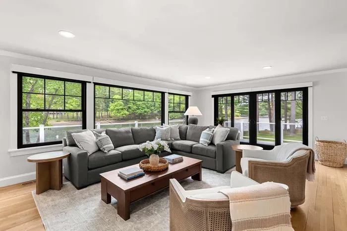 The heart of the home. A sprawling sectional, smart TV, and two lounge chairs — plus sliders that blur the line between inside and out, opening to a stunning creekside deck