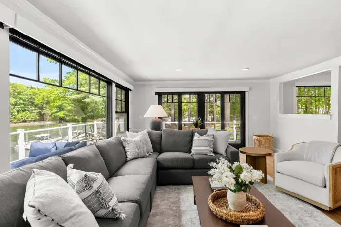 The heart of the home. A sprawling sectional, smart TV, and two lounge chairs — plus sliders that blur the line between inside and out, opening to a stunning creekside deck