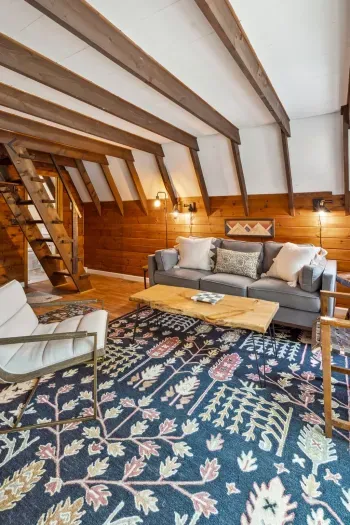 The living area with a full size couch, additional chairs, access to the deck, Smart TV, and mini split heating and cooling! Access to the upstairs bedrooms is pictured via the stairs/ladder