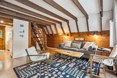 The living area with a full size couch, additional chairs, access to the deck, Smart TV, and mini split heating and cooling! Access to the upstairs bedrooms is pictured via the stairs/ladder