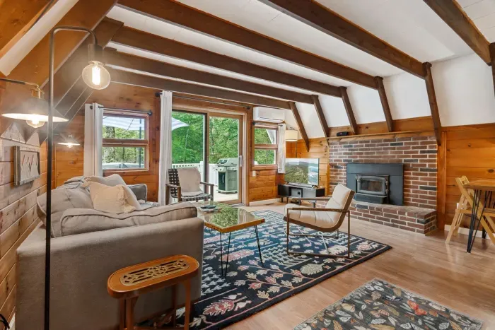 The living area with a full size couch, additional chairs, access to the deck, Smart TV, and mini split heating and cooling! Access to the upstairs bedrooms is pictured via the stairs/ladder