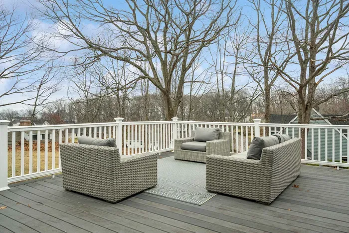 Expansive rear deck with gray wicker lounge seating, a dining area, and tranquil wooded views.