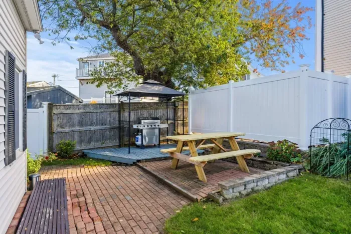 Patio in side yard with outdoor grill and picnic table.