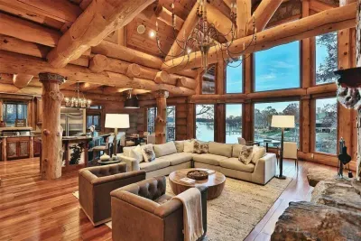 Soaring timber ceilings, a grand stone fireplace, and floor-to-ceiling windows with lake views define this stunning great room—designed for gathering, relaxing, and taking in the beauty of the water.