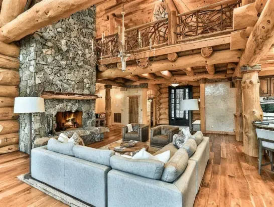 This elegant lodge-style great room blends rustic craftsmanship with modern comfort, featuring a massive stone fireplace, plush seating, and an open layout ideal for group gatherings.