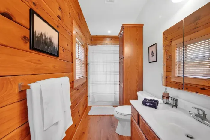 Upstairs primary bath with exposed wood wall and features soap, shampoo, conditioner and bodywash.  Includes handrail for entering/exiting the shower.