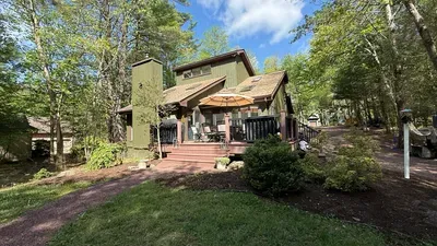 Back of the home where theres a deck, patio table with sun umbrella and seating for 8 - there's also a BBQ grill and some games.