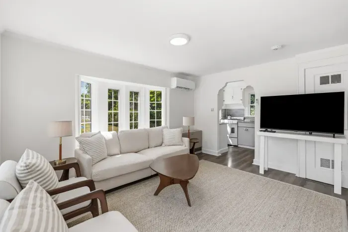 Bright living room with big windows, plush seating, TV, and kitchen access