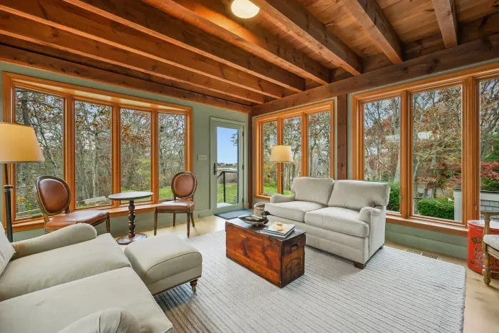 Sunlit living room with exposed beams and serene woodland views
