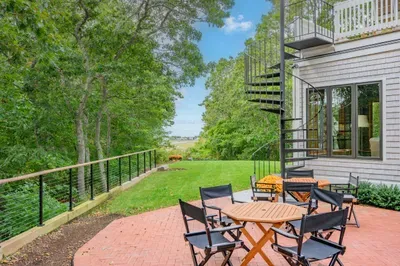 Private tree-lined patio with lawn, balcony access, and distant water views