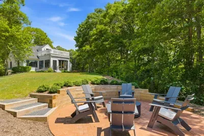 Private backyard fire pit patio surrounded by trees and open lawn