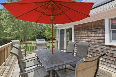 Private deck with outdoor dining, red umbrella, and peaceful wooded views
